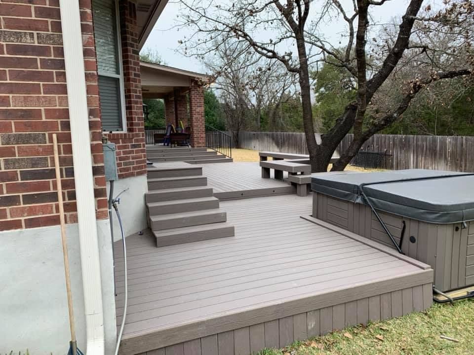 Multi-level gray composite deck with wide steps, built-in bench, and a hot tub
