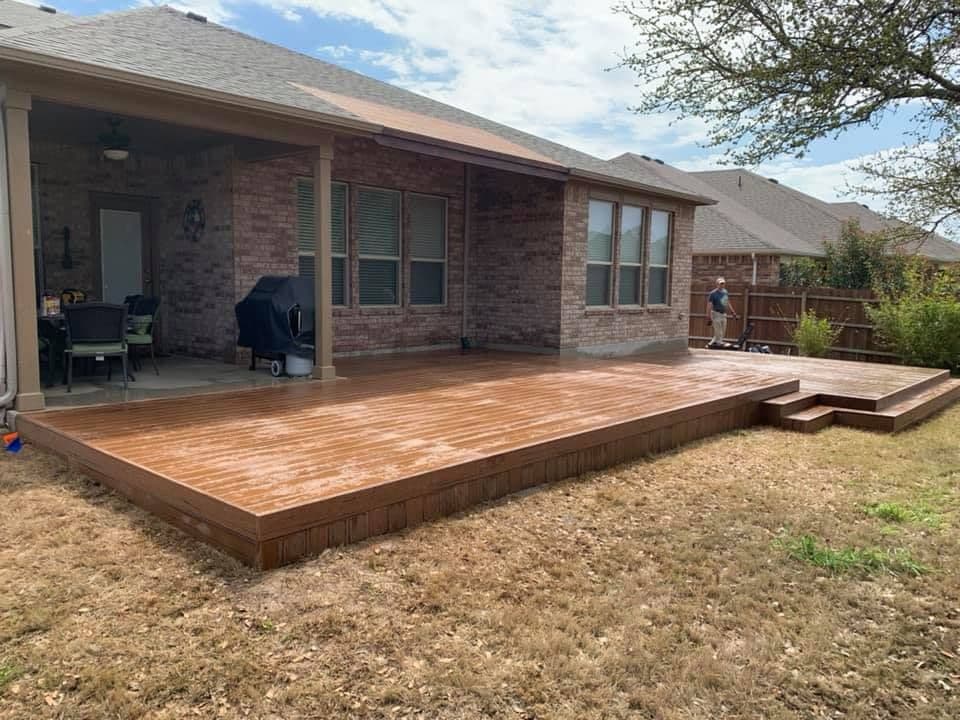 Ground-level brown composite deck extending a covered patio across the back of a brick home