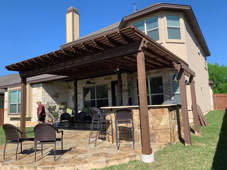Stained wood pergola over a flagstone patio with a stone outdoor bar and ceiling fan