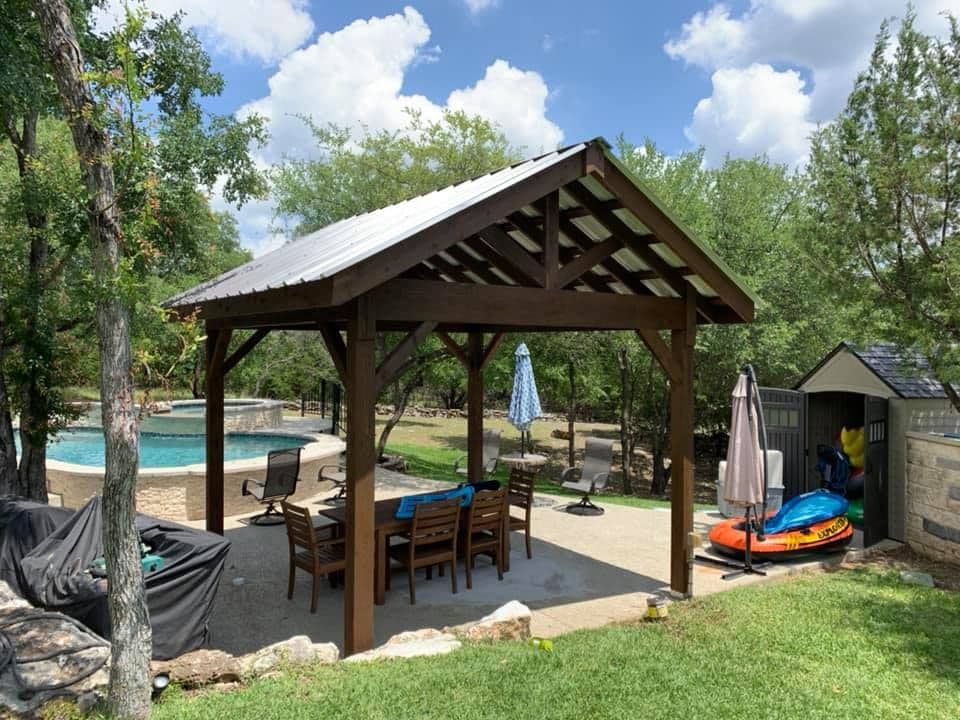 Timber-frame pavilion with a metal gable roof shading a dining patio beside a backyard pool