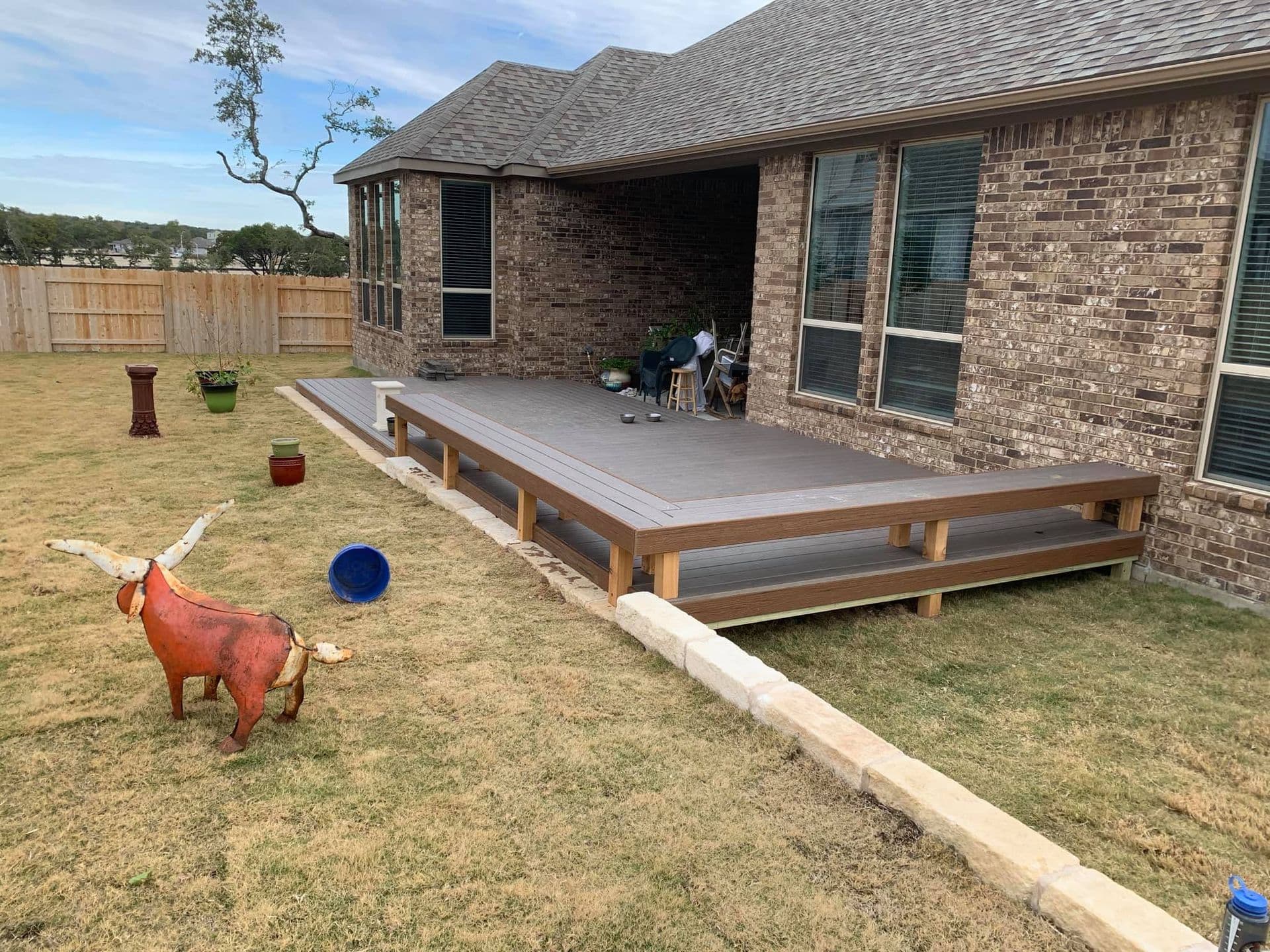 Wraparound composite deck with built-in perimeter bench seating along a Central Texas brick home
