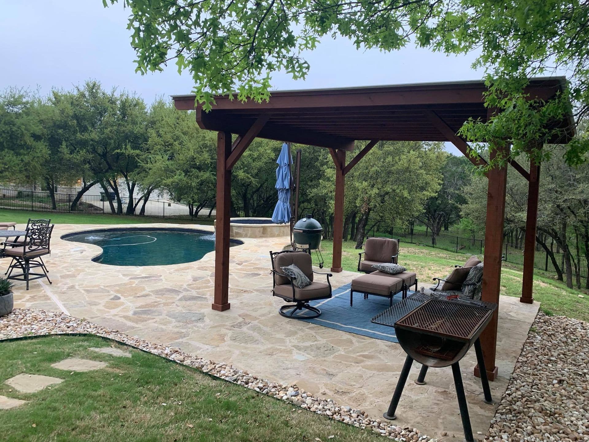 Stained cedar pavilion over a flagstone patio next to a pool and hill country oaks
