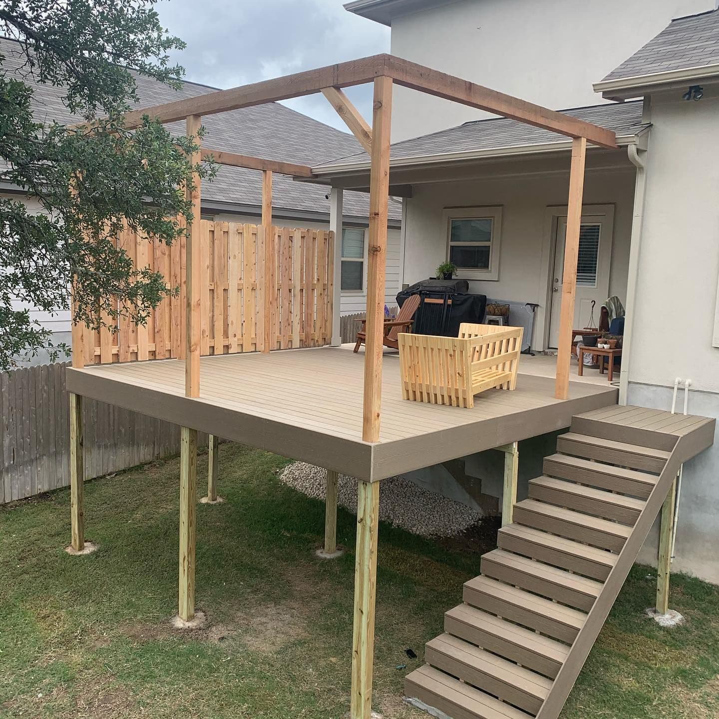 Raised composite deck with cedar pergola frame, privacy screen, and full-width stairs in the Austin area