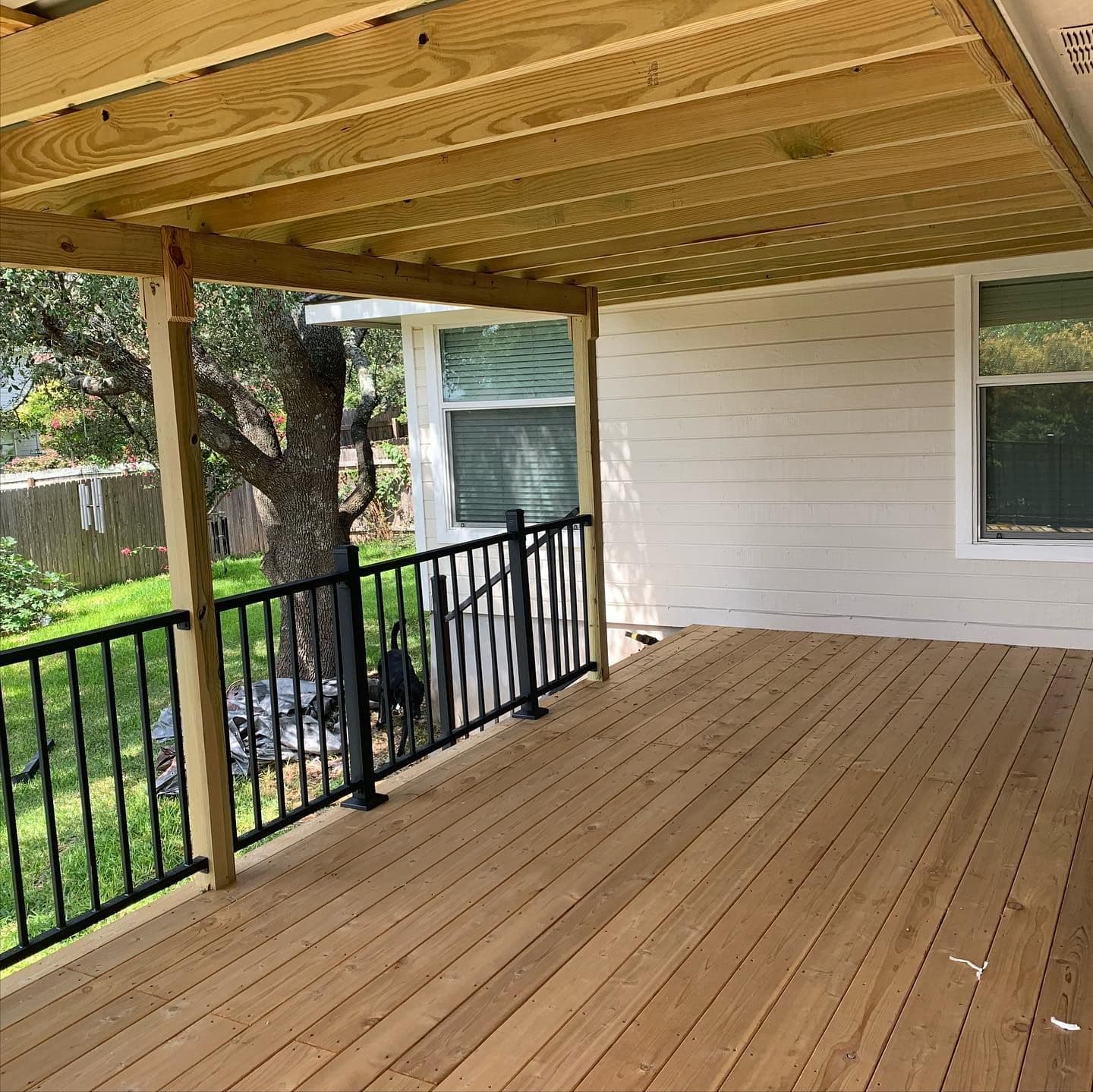 New covered wood deck with exposed rafters and black metal railing under a mature oak