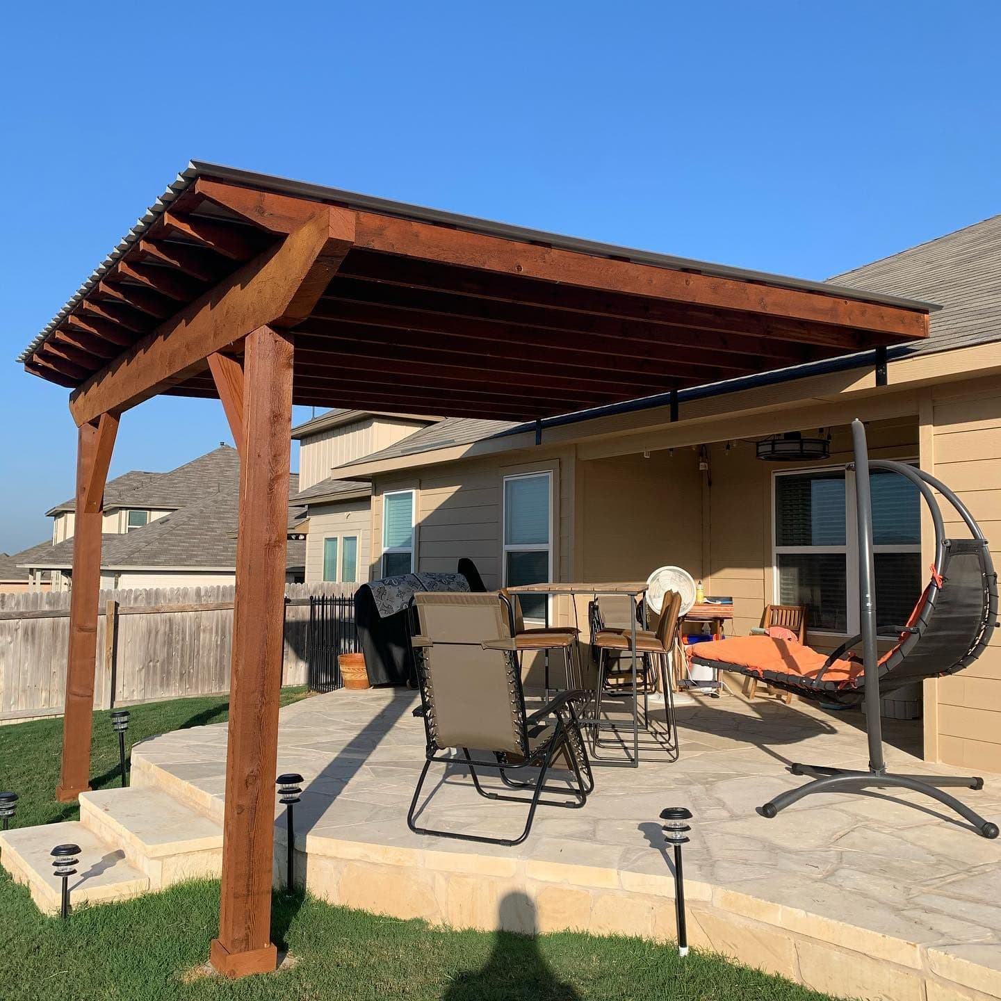 Cedar patio cover with metal roof over a raised flagstone patio in a Central Texas backyard
