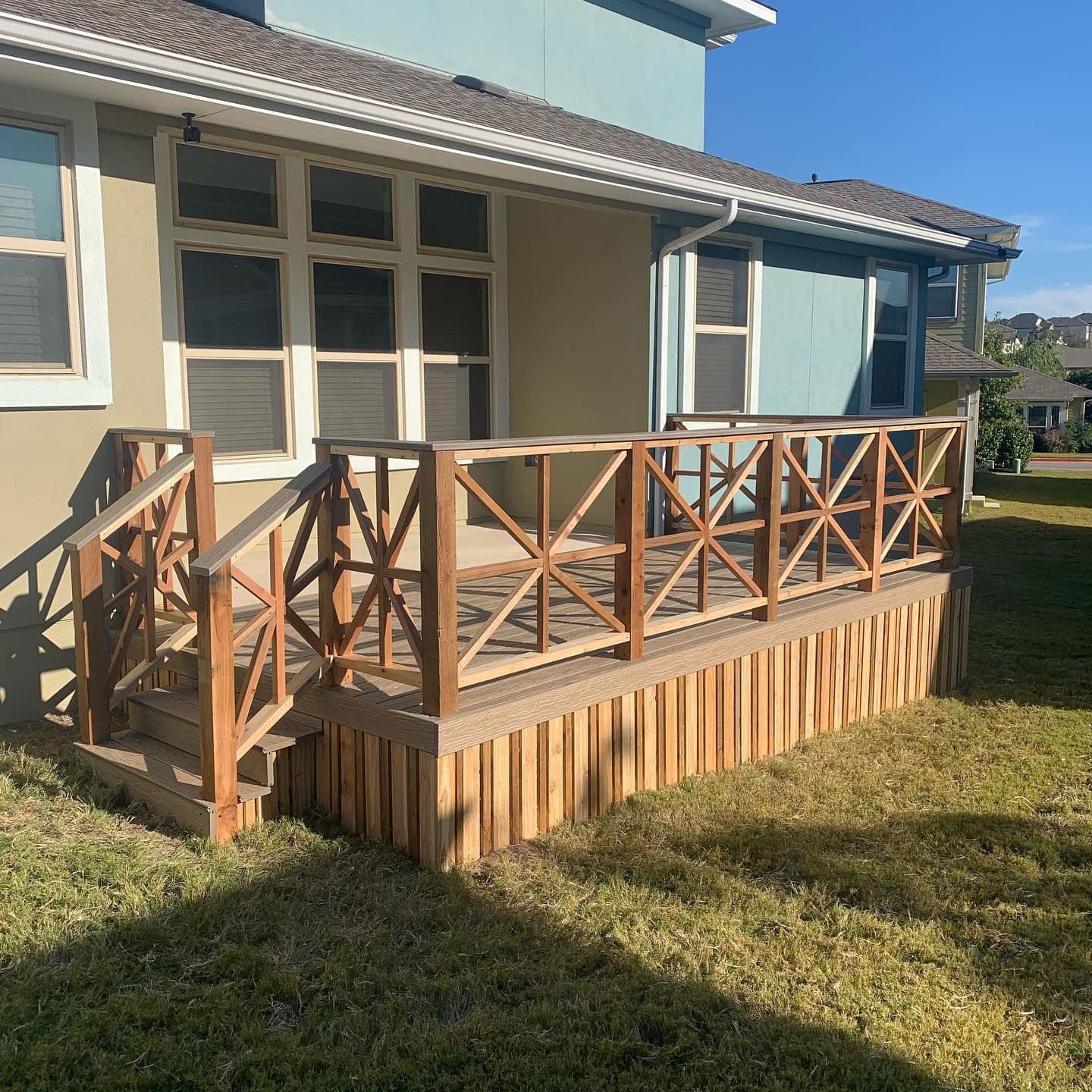 Cedar deck with decorative crisscross wood railings and vertical board skirting around the base