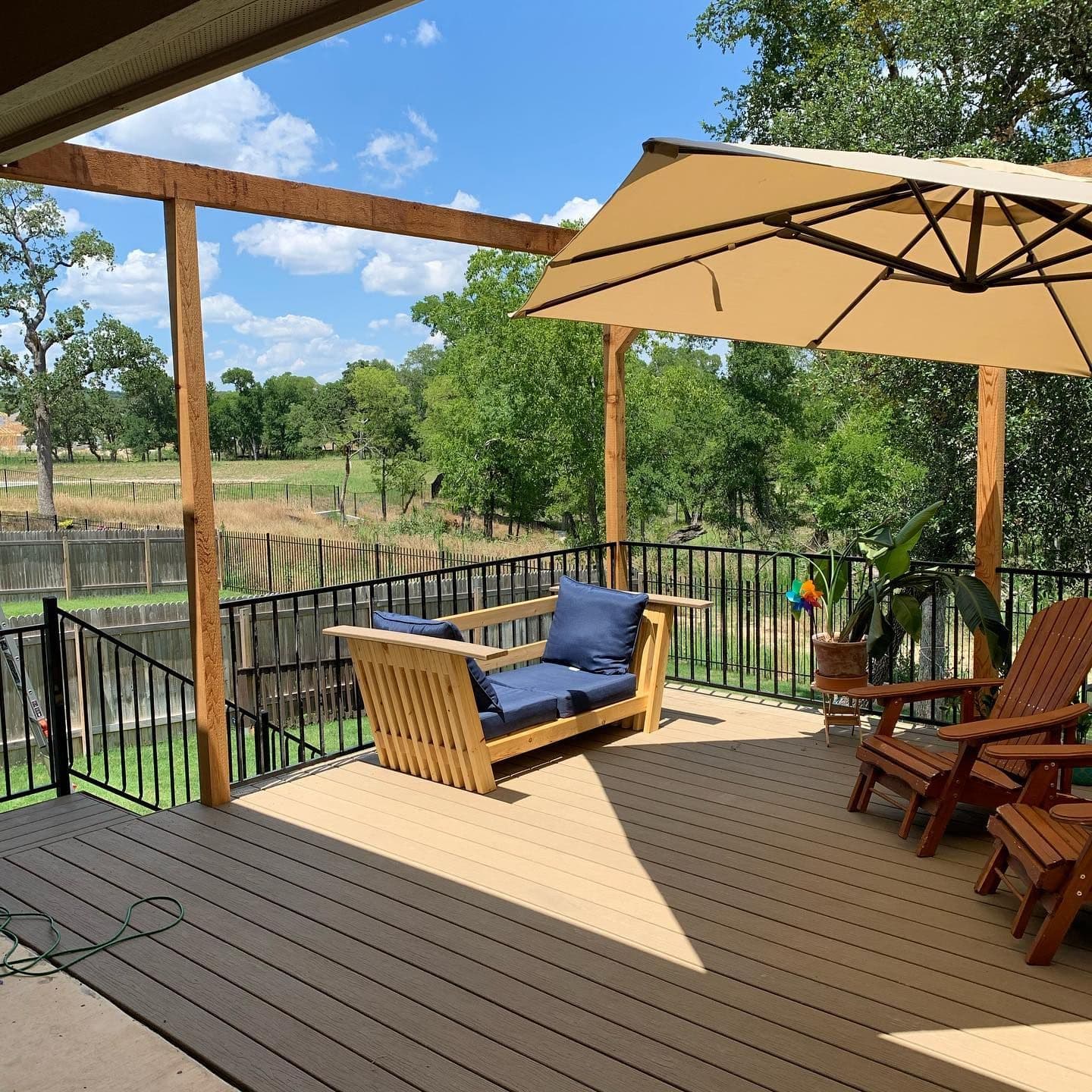 Covered composite deck with cedar posts, black metal railing, and a hanging daybed swing
