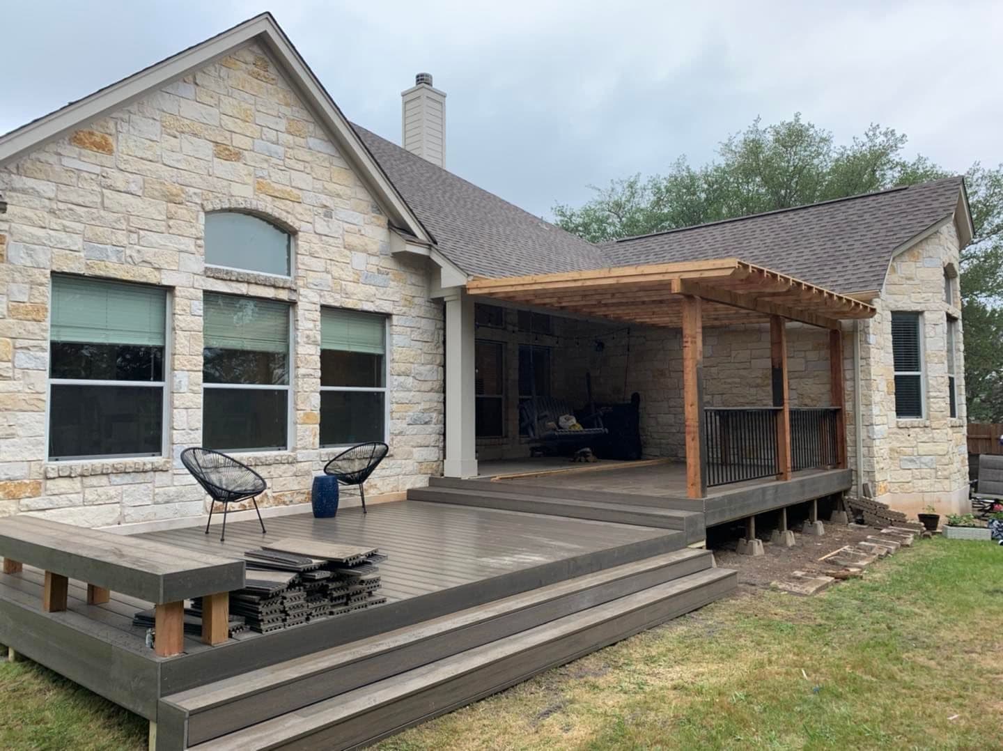 Multi-level gray composite deck with wide steps, built-in bench, and cedar pergola on a limestone home