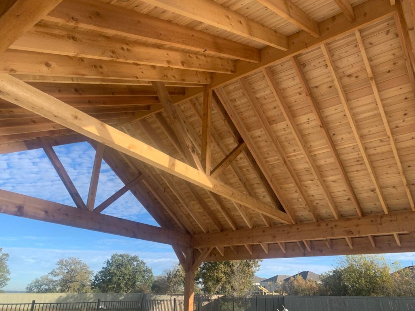 Tongue-and-groove cedar ceiling and exposed timber trusses inside an open-gable pavilion