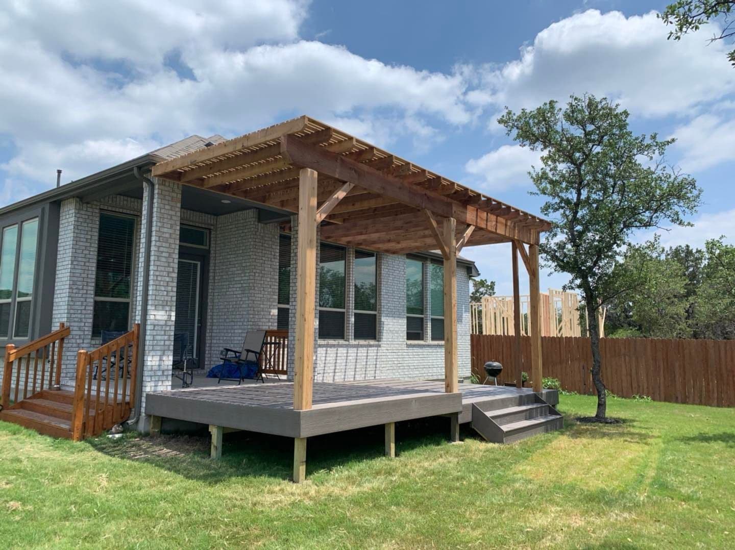 Raised composite deck with a stained cedar pergola and side stairs on a white brick home