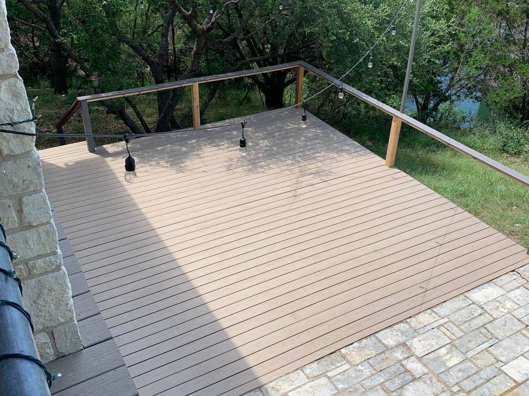 Composite deck with cedar top rail and string lights beside a limestone wall and wooded creek