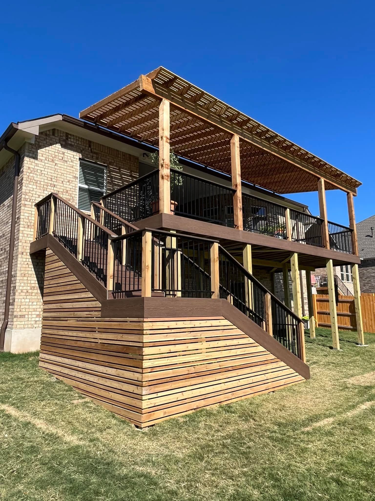 Second-story composite deck with cedar pergola, black railing, and horizontal wood stair skirting