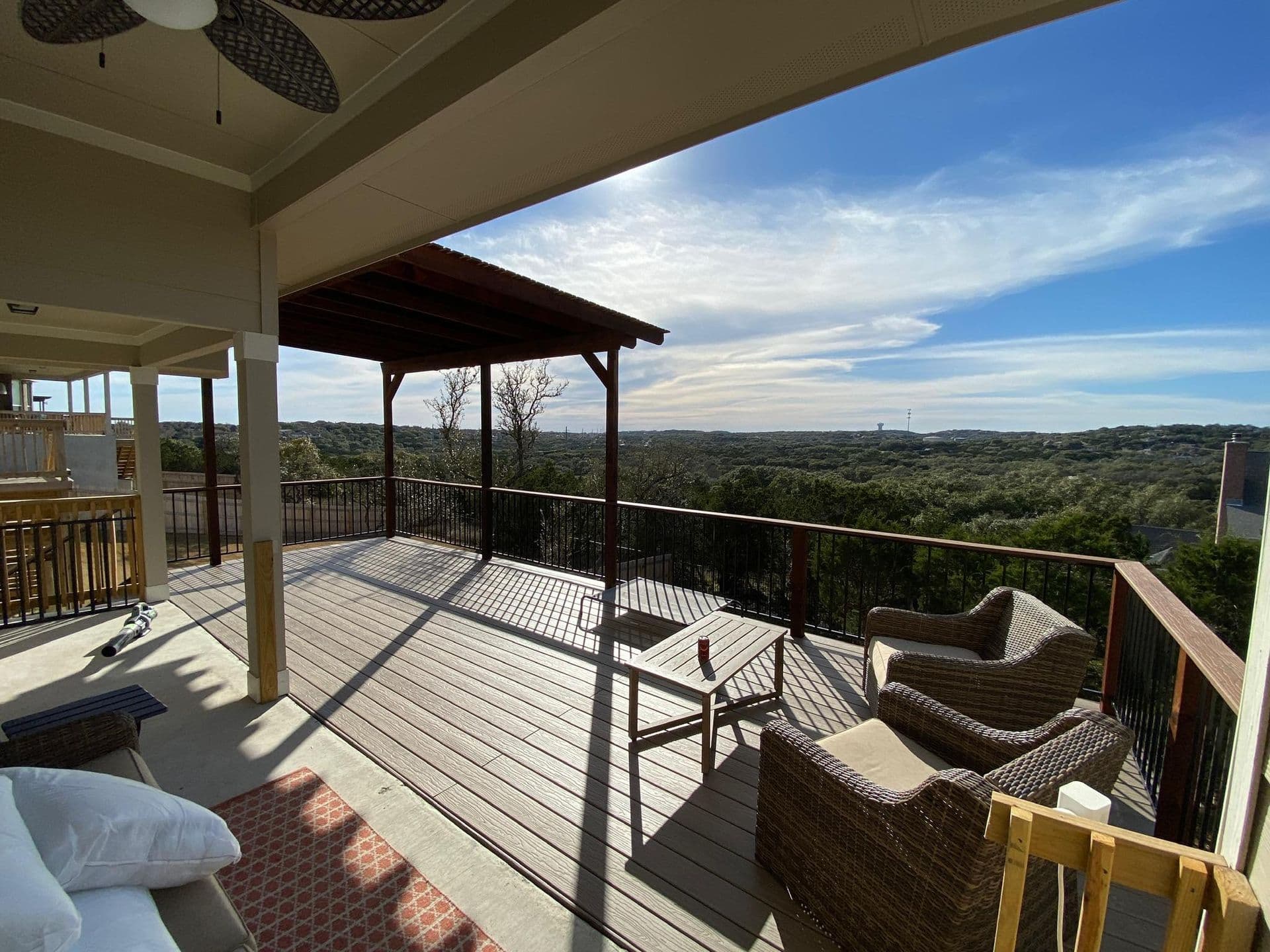 Elevated covered deck with ceiling fan, attached pergola, and black railing over Austin area hills