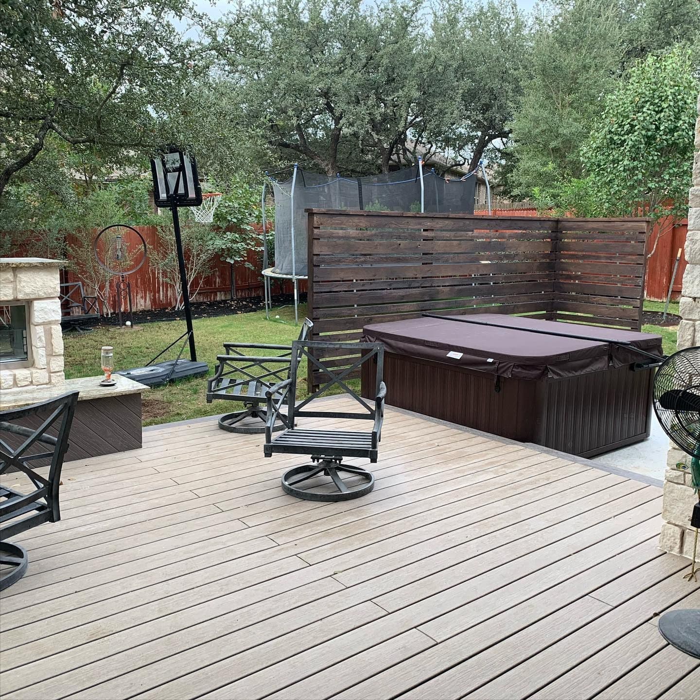 Composite deck with a hot tub, stained horizontal privacy screen, and stone fireplace edge