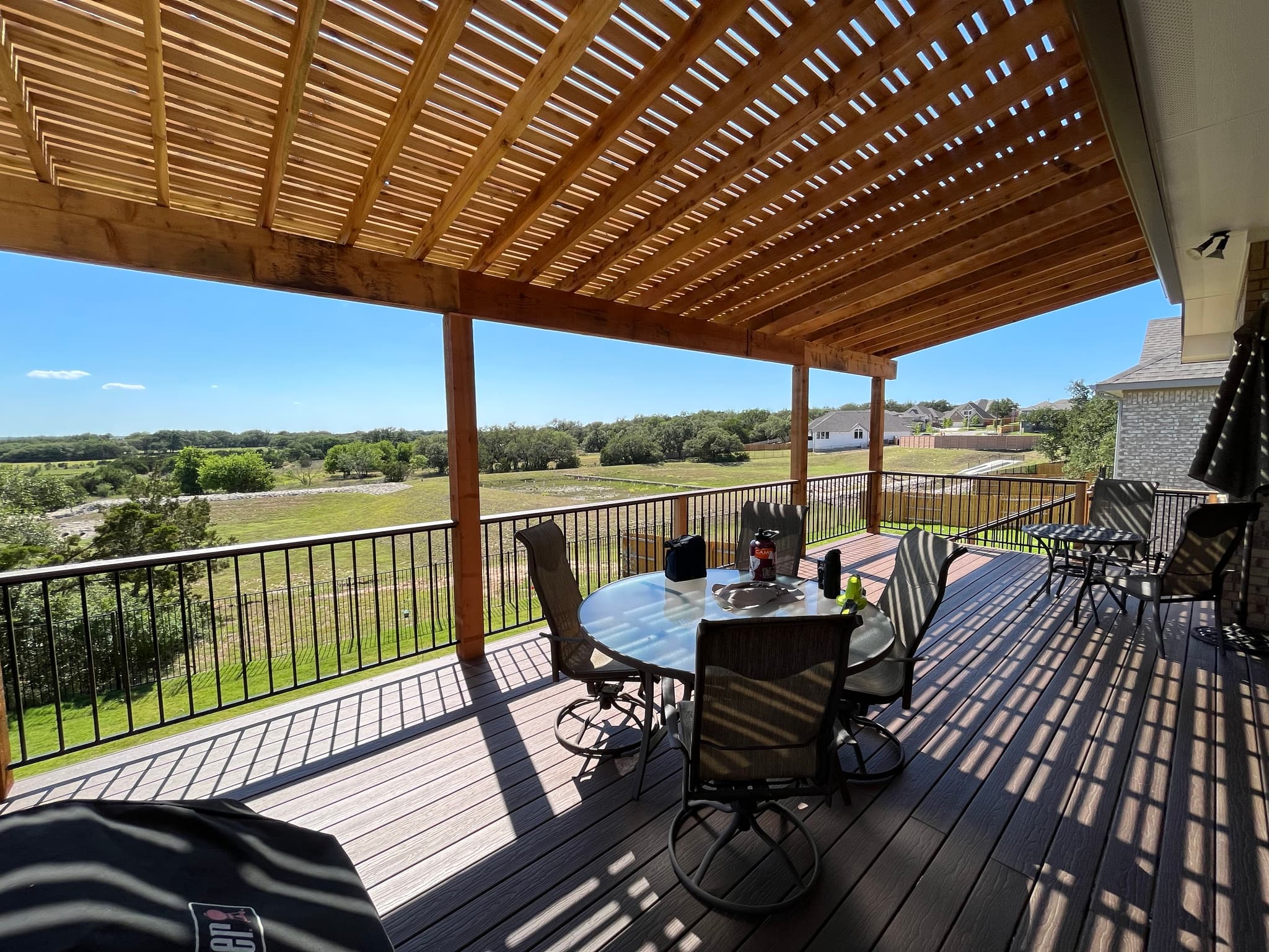 Slatted cedar pergola roof casting shade over a composite deck with patio dining and field views