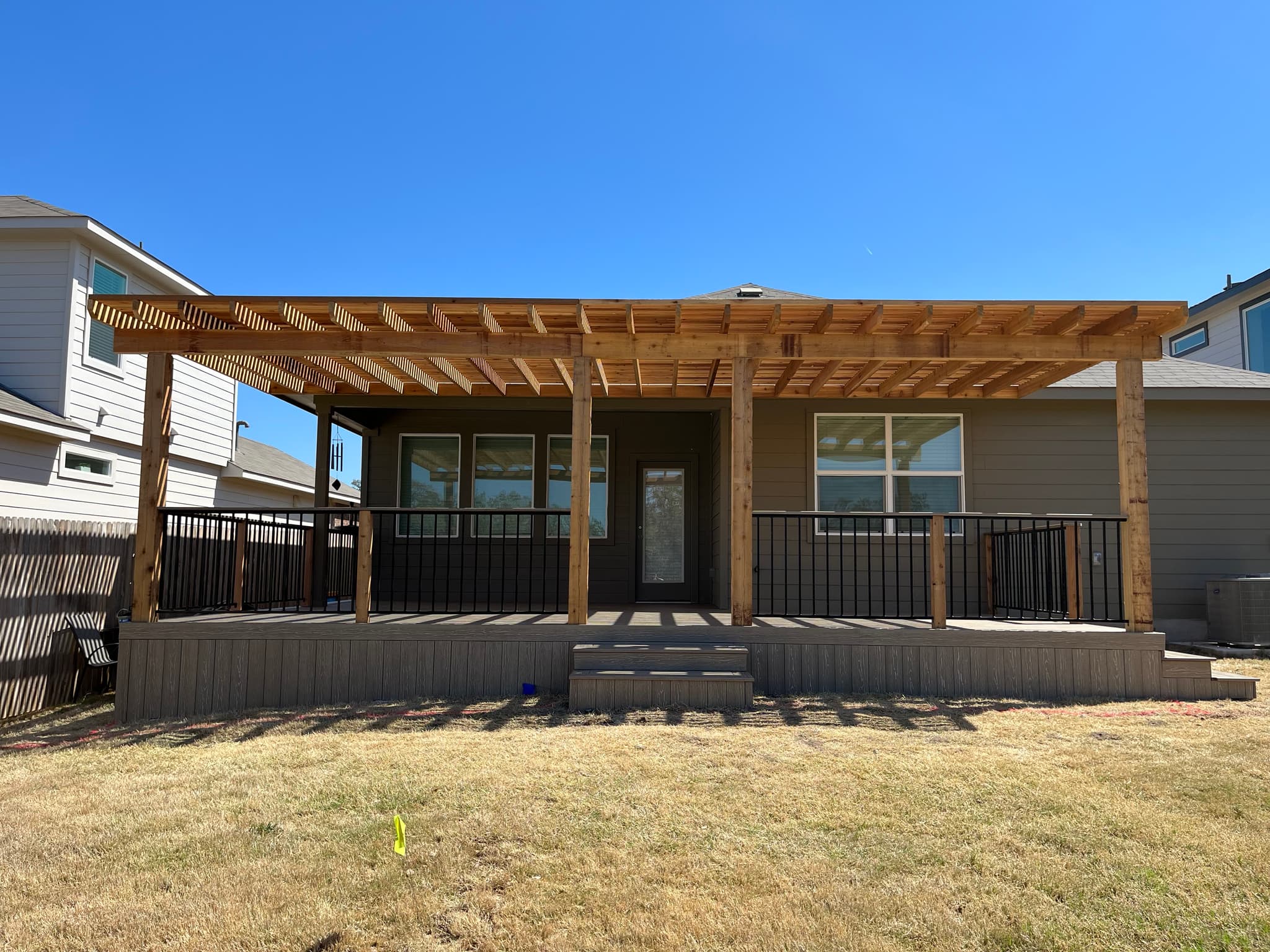 Full-width cedar pergola over a low composite deck with black railing on a Central Texas home